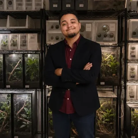 Dusty Mumphrey standing with arms crossed in front of racks of reptile enclosures