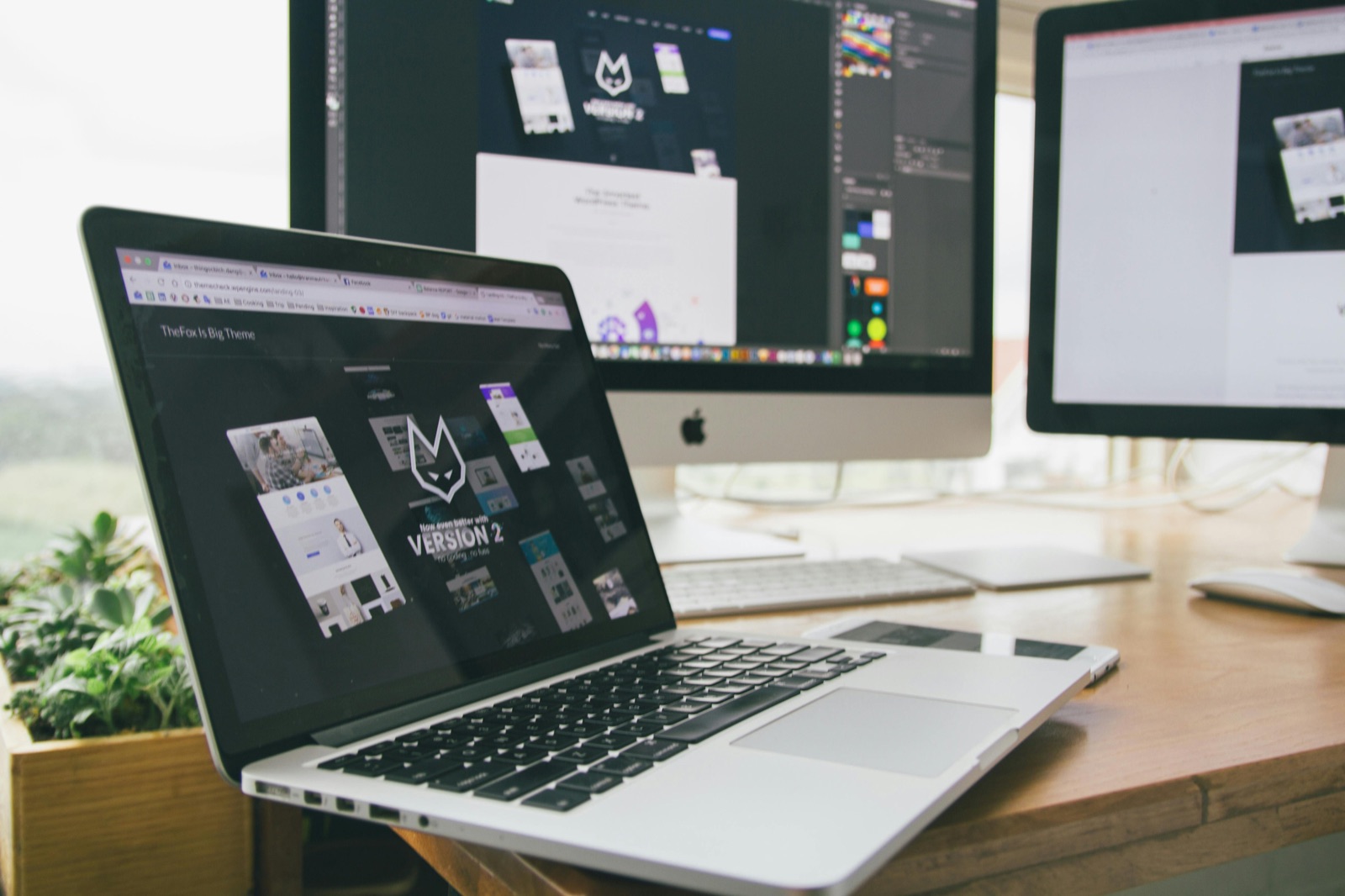A laptop and two desktop monitors showing website designs