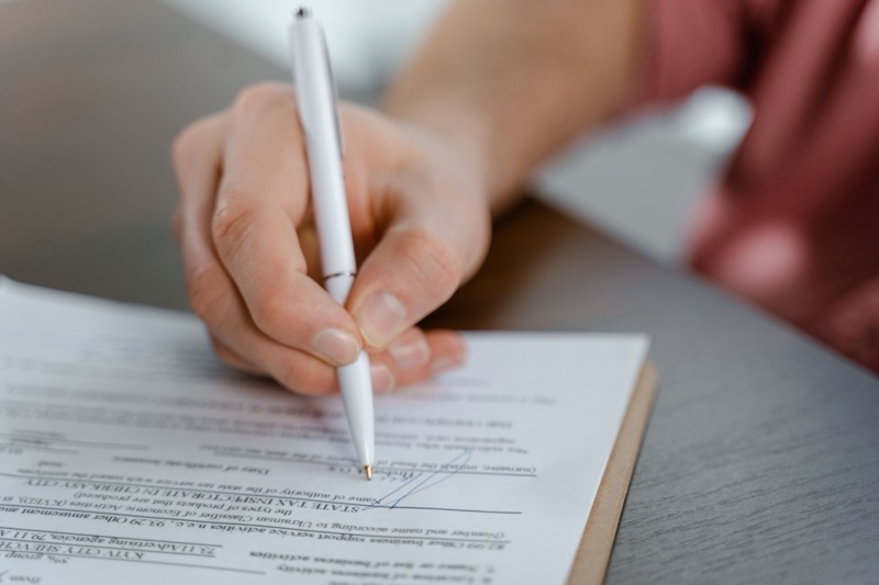 A hand signing a printed contract with a white pen