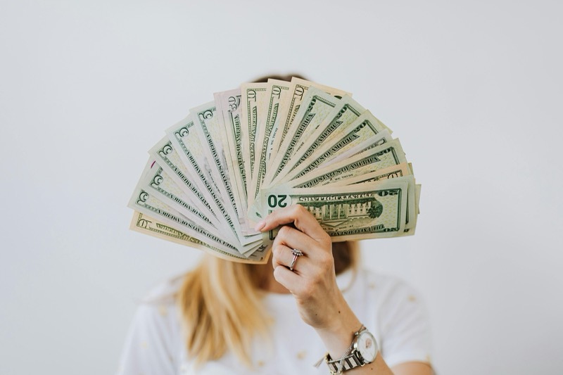 A person holding a fan of dollar bills in front of their face