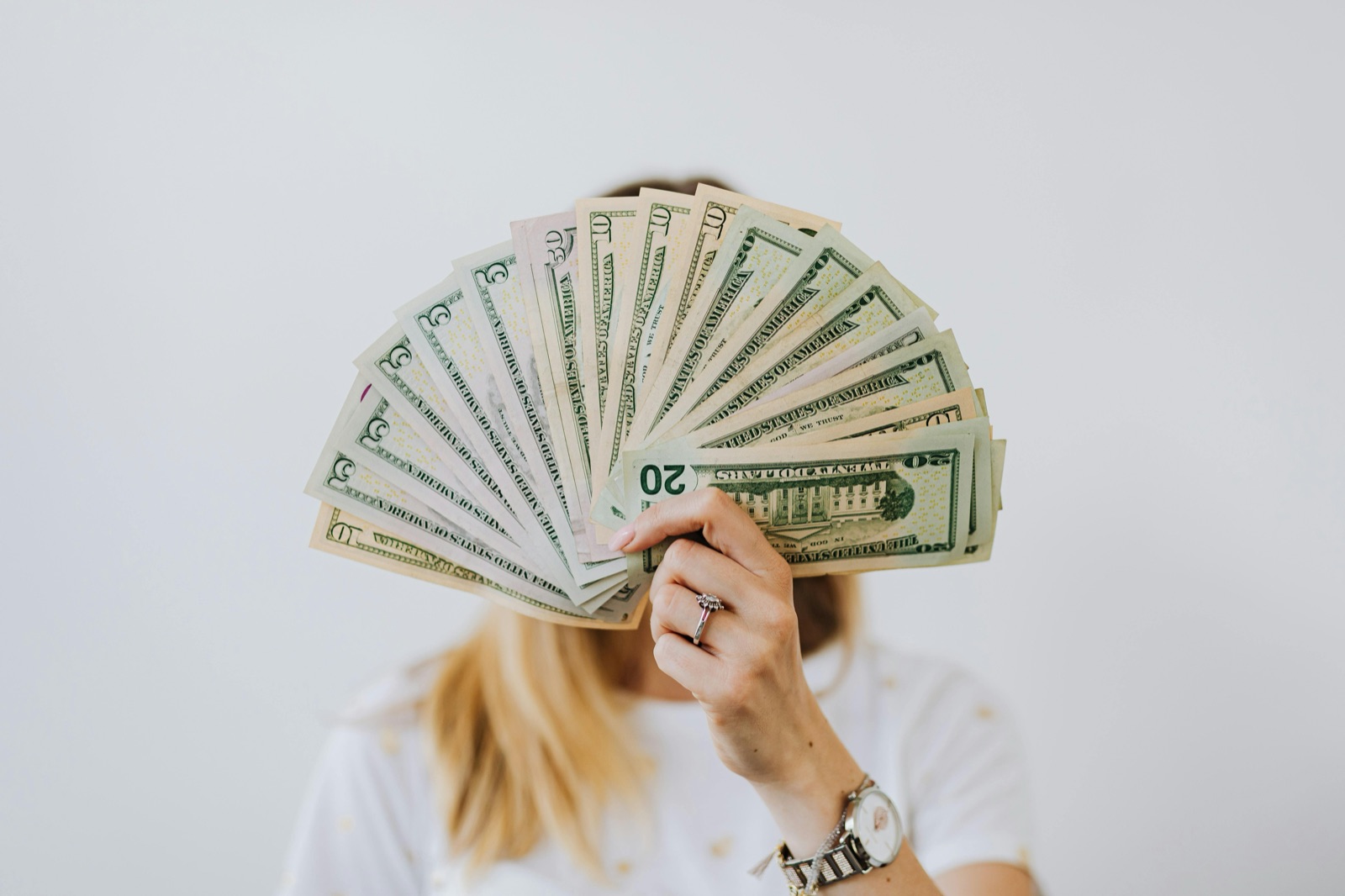 A person holding a fan of dollar bills in front of their face