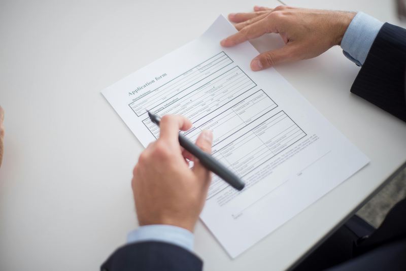 A hand holding a pen over a printed application form