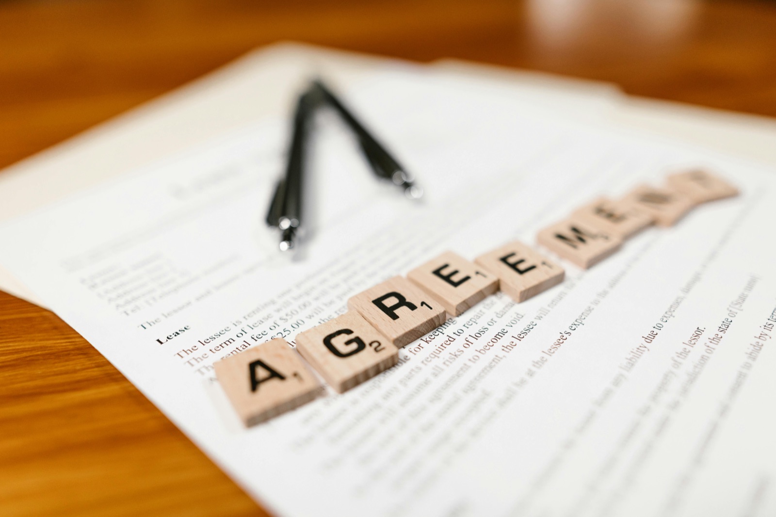 Letter tiles spelling AGREEMENT on a printed contract beside a pen