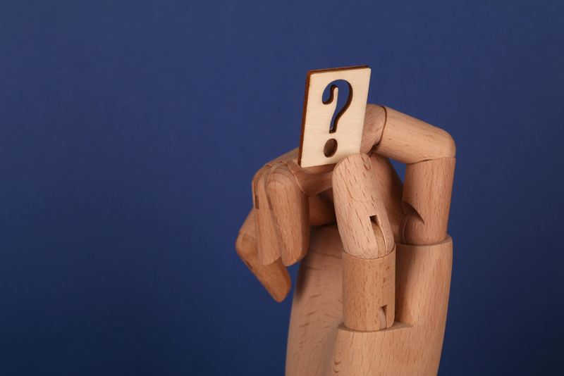 A wooden mannequin hand holding a card with a question mark